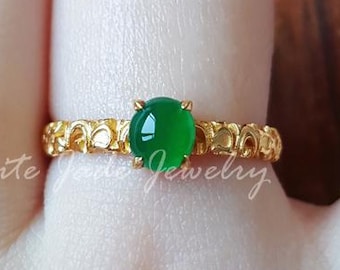 May include: A gold ring with a green jadeite gemstone. The ring has a detailed design with a textured band.