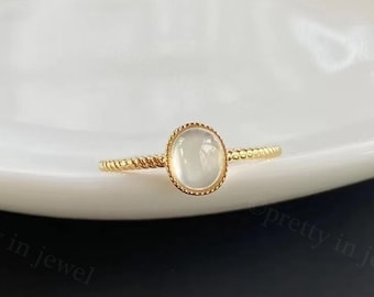 May include: A gold ring with a white oval gemstone. The ring has a twisted band.