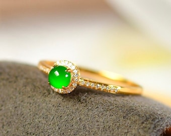 Peut inclure: Une bague en or avec une pierre précieuse en jade vert entourée d'un halo de petits diamants.