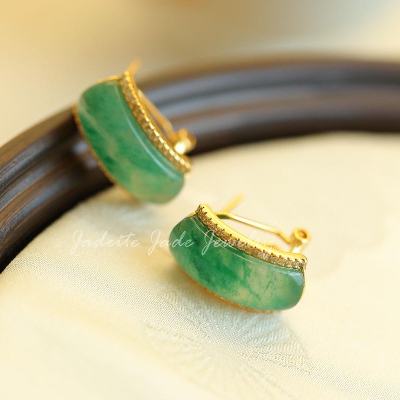 Pu&ograve; includere: Un paio di orecchini di giada con finiture dorate. Gli orecchini sono di un vibrante colore verde e hanno una forma rettangolare curva. Il testo "Jadeite Jade Jewelry" &egrave; visibile nell'immagine.