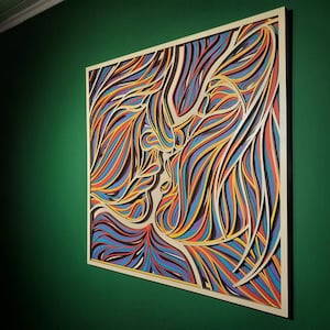 May include: A colorful abstract art piece featuring two figures in a close embrace. The artwork is made of layered paper cutouts in shades of blue, red, yellow, and brown.