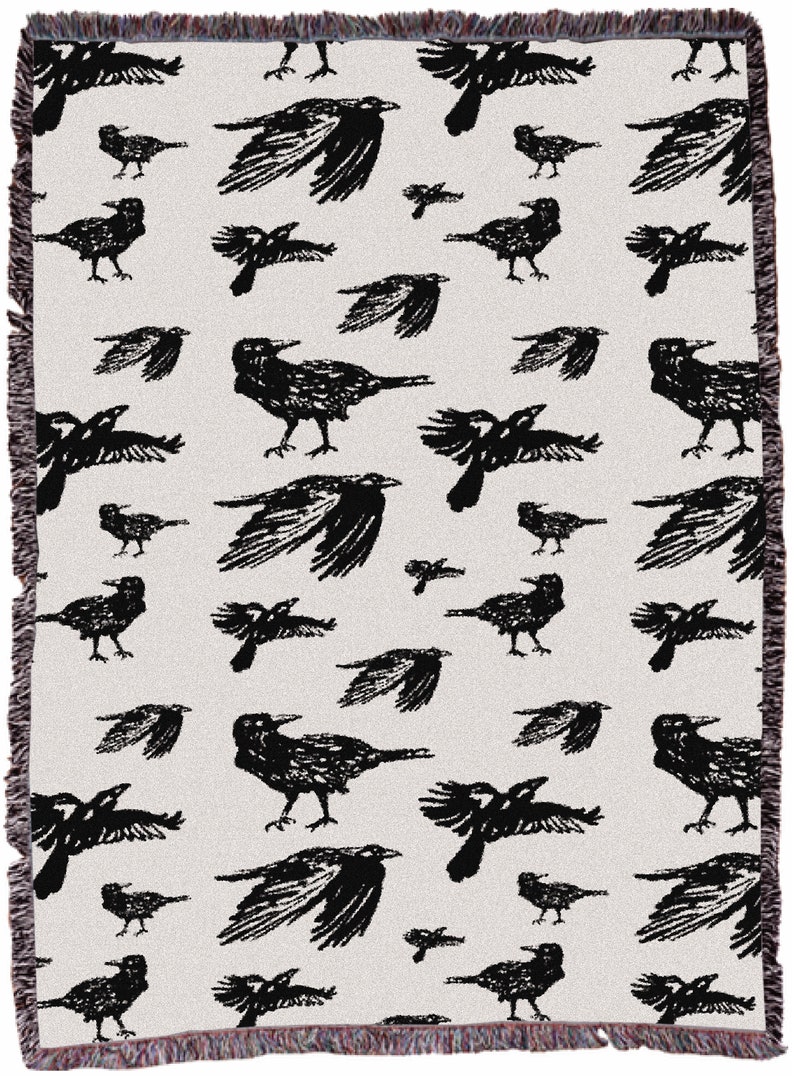 May include: A woven throw blanket featuring a repeating pattern of black birds on a cream background. The birds are shown in different poses, some with wings outstretched. The blanket has a fringed edge.