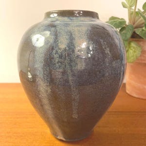 May include: A handcrafted ceramic vase with a dark blue and brown glaze. The vase has a rounded body and a narrow neck. The glaze has a glossy finish and a unique, textured appearance. This decorative vase is suitable for displaying flowers or as a standalone art piece.