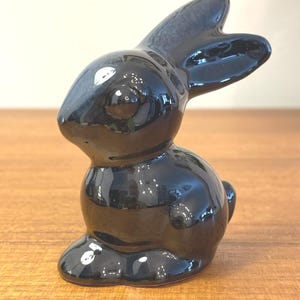 May include: A glossy black ceramic bunny figurine. The bunny is in a seated position with its ears perked up. The figurine has a smooth, reflective surface, and is a decorative item.