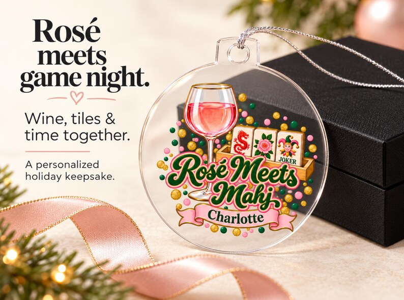 Op de afbeelding: Een doorzichtig, rond, plat ornament met een afbeelding van een wijnglas gevuld met roze vloeistof, drie mahjongtegels en de tekst "Ros&eacute; Meets Mahj" boven een roze banner met de naam "Charlotte" in het zwart, geaccentueerd door kleurrijke stippen.