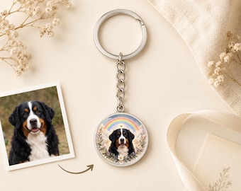 May include: A circular metal keyring featuring a custom illustration of a Bernese Mountain Dog centred beneath a colourful rainbow. The dog has black, white, and brown fur. The keyring includes a silver-toned split ring and a short chain link.
