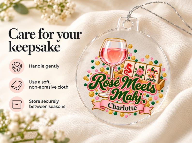 Op de afbeelding: Een ronde, transparante acryl hanger met een afbeelding van een wijnglas met roze vloeistof, drie mahjongtegels en de tekst "Ros&eacute; Meets Mahj" boven een roze banner met de naam "Charlotte" in zwarte letters, hangend aan een zilverkleurig koord.