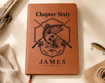 May include: A tan leather-bound journal featuring a black engraved design of a fish jumping out of water, crossed fishing rods, and the text Chapter Sixty and JAMES. The cover has a smooth texture and a rectangular shape with rounded corners.