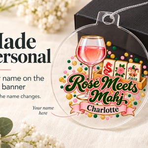 Op de afbeelding: Een doorzichtige ronde acryl hanger met een afbeelding van een wijnglas met roze inhoud, een houten rekje met mahjongtegels en verspreide groene, roze en gouden stippen. De tekst Rose Meets Mahj staat boven een roze banner met de naam Charlotte.