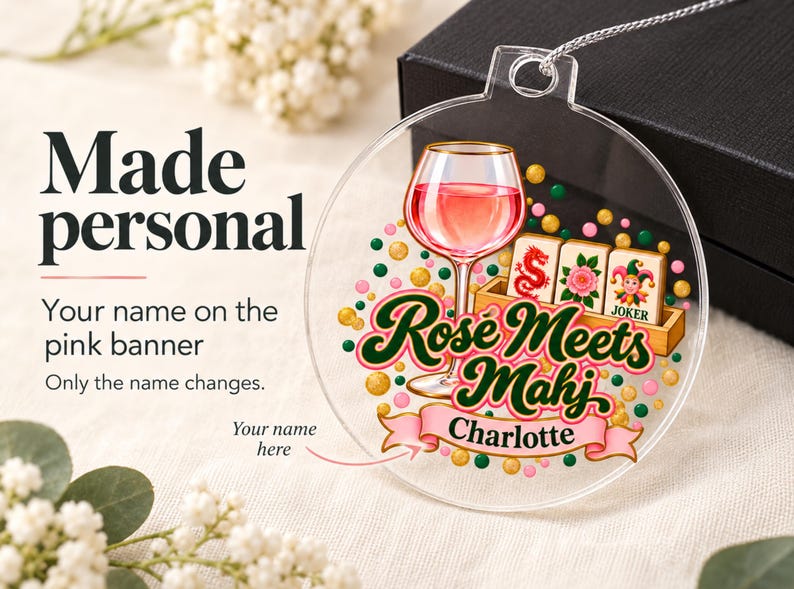 Op de afbeelding: Een doorzichtige ronde acryl hanger met een afbeelding van een wijnglas met roze inhoud, een houten rekje met mahjongtegels en verspreide groene, roze en gouden stippen. De tekst Rose Meets Mahj staat boven een roze banner met de naam Charlotte.