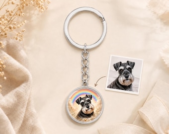 May include: A silver-toned metal keyring featuring a circular pendant with a printed image of a black and grey Schnauzer dog set against a background of wheat stalks and a rainbow. A small square photograph of the same dog is positioned nearby.