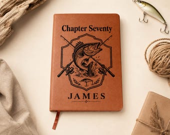 May include: A tan leather-bound journal featuring a black engraved design of a fish jumping between two crossed fishing rods inside a shield emblem. The text "Chapter Seventy" appears above the emblem, and the name "JAMES" is printed below.