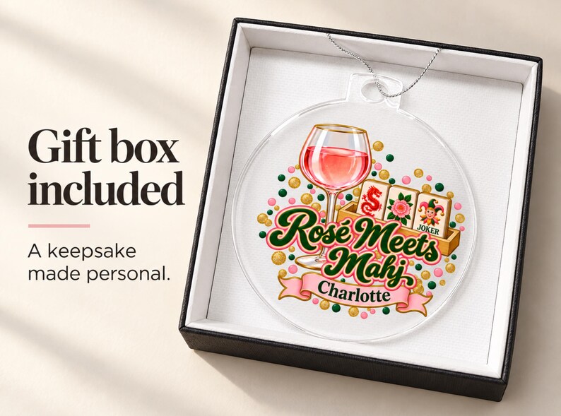 Op de afbeelding: Een ronde, doorzichtige acryl hanger met een afbeelding van een wijnglas, mahjongtegels en de tekst "Ros&eacute; Meets Mahj" met de naam "Charlotte" op een roze lint, gepresenteerd in een zwarte geschenkdoos met een witte binnenkant.