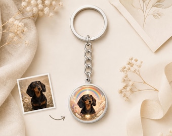 May include: A silver keychain featuring a circular pendant with a custom illustration of a black and tan dachshund dog set against a rainbow and floral background, accompanied by a small square photograph of the same dog breed.