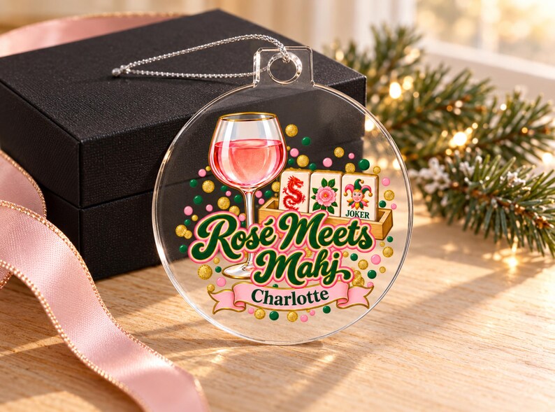 Op de afbeelding: Een doorzichtige, ronde acryl hanger met een afbeelding van een glas ros&eacute;wijn, drie mahjongtegels en de tekst "Ros&eacute; Meets Mahj" boven een roze lint met de naam "Charlotte" in zwarte letters, versierd met kleurrijke confetti stippen.