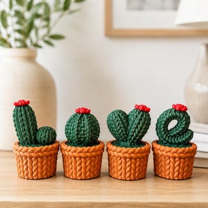 Peut inclure: Quatre figurines de cactus verts dans des pots orange à texture tricotée, disposées pour épeler le mot LOVE. Chaque cactus porte une petite fleur rouge au sommet, les cactus formant les lettres L, O, V et E sur une surface en bois.
