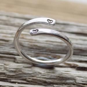 May include: A silver ring with two small heart engravings. The ring is made of a thick band of metal and is twisted into a spiral shape.
