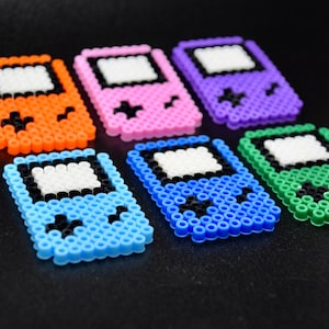 May include: Six colorful pixel art Game Boy style keychains. The keychains are made of plastic beads and feature different colors, including orange, pink, purple, blue, green, and light blue.