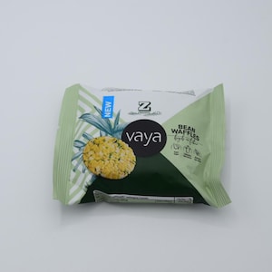 Könnte beinhalten: Eine grün-weiße Packung Vaya Bean Waffles mit einem Ananas-Design und dem Text "NEW" und "BEAN WAFFLES" auf der Vorderseite.