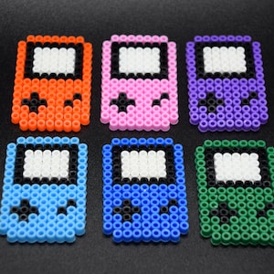 May include: Six colorful pixel art game consoles made with perler beads. The consoles are orange, pink, purple, blue, light blue, and green.