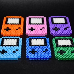 May include: Six colorful pixel art game console keychains. The keychains are made of plastic beads and feature different colors, including orange, pink, purple, blue, and green.