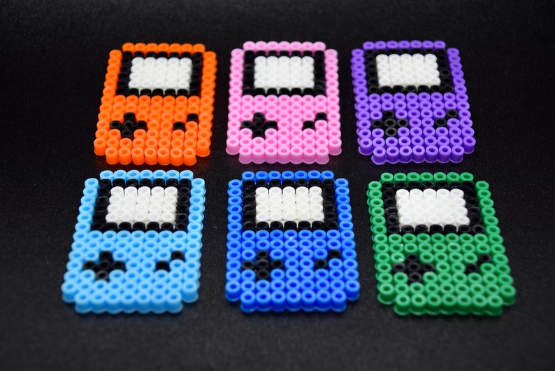 May include: Six colorful pixel art game consoles made with perler beads. The consoles are orange, pink, purple, blue, green, and light blue.