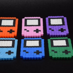May include: Six colorful pixel art Game Boy style keychains. The keychains are made of plastic beads and come in orange, pink, purple, blue, light blue, and green.