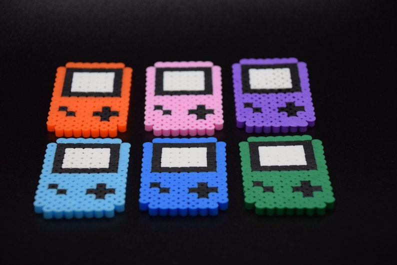 May include: Six colorful pixel art Game Boy style keychains. The keychains are made of plastic beads and come in orange, pink, purple, blue, light blue, and green.