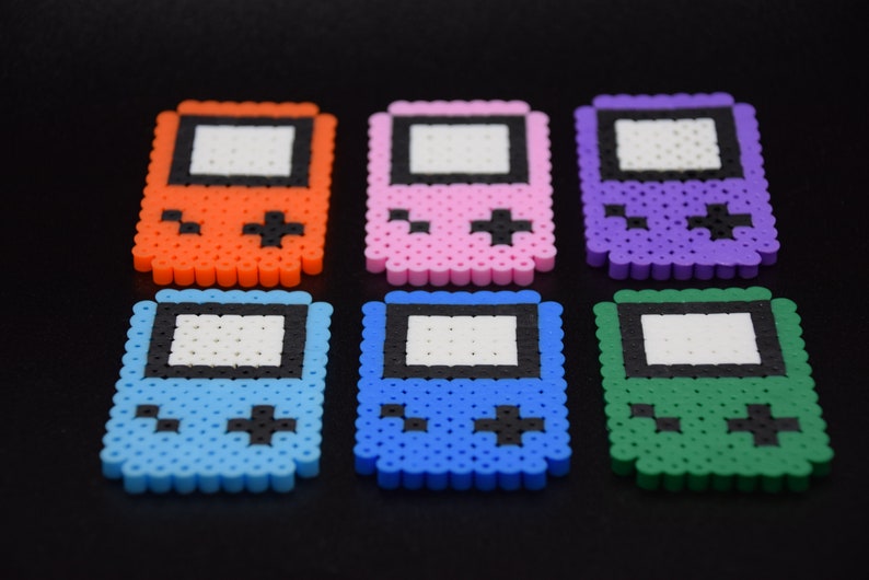 May include: Six colorful pixel art game console keychains. The keychains are made of plastic beads and feature a variety of colors, including orange, pink, purple, blue, light blue, and green.