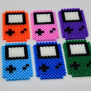May include: Six colorful pixel art Game Boy style keychains. The keychains are made of plastic beads and come in orange, pink, purple, blue, light blue, and green.