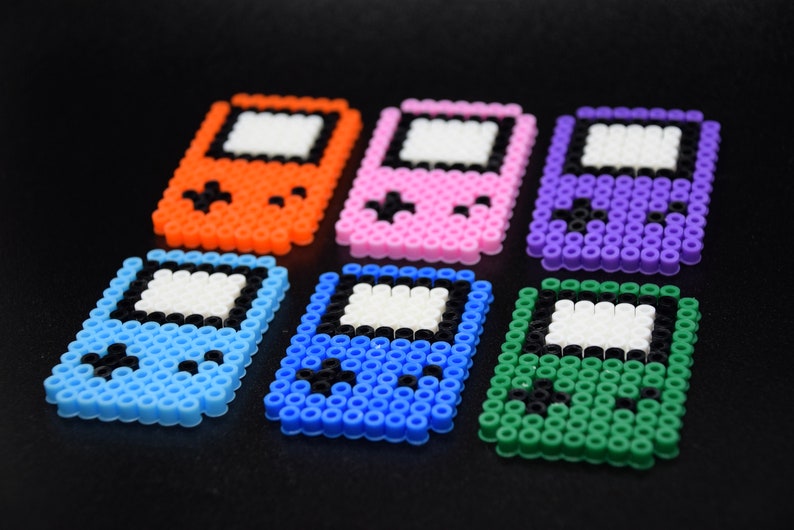 May include: Six colorful pixel art game consoles made with perler beads. The consoles are in orange, pink, purple, blue, green, and light blue.