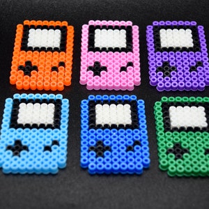 May include: Six colorful pixel art game console keychains. The keychains are made of plastic beads and feature different colors, including orange, pink, purple, blue, and green.