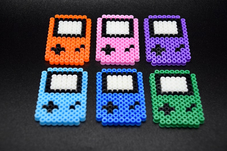May include: Six colorful pixel art game console keychains. The keychains are made of plastic beads and feature different colors, including orange, pink, purple, blue, and green.