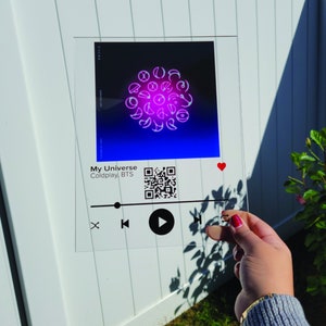 May include: A clear acrylic sign with a black and white Spotify-style music player design. The sign features a pink and purple graphic of a circle with various symbols inside. The text "My Universe Coldplay, BTS" is displayed on the sign. A QR code is also included.