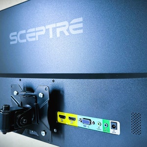 May include: The back of a black Sceptre monitor with a black arm mount. The monitor has a variety of ports including HDMI, VGA, and audio out.