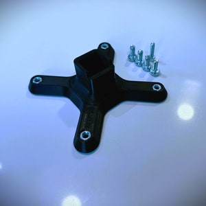 Pode incluir: Uma base de pl&aacute;stico preto com quatro bra&ccedil;os e um furo quadrado no centro. A base &eacute; projetada para ser fixada a uma superf&iacute;cie com parafusos. Inclui cinco parafusos prateados.