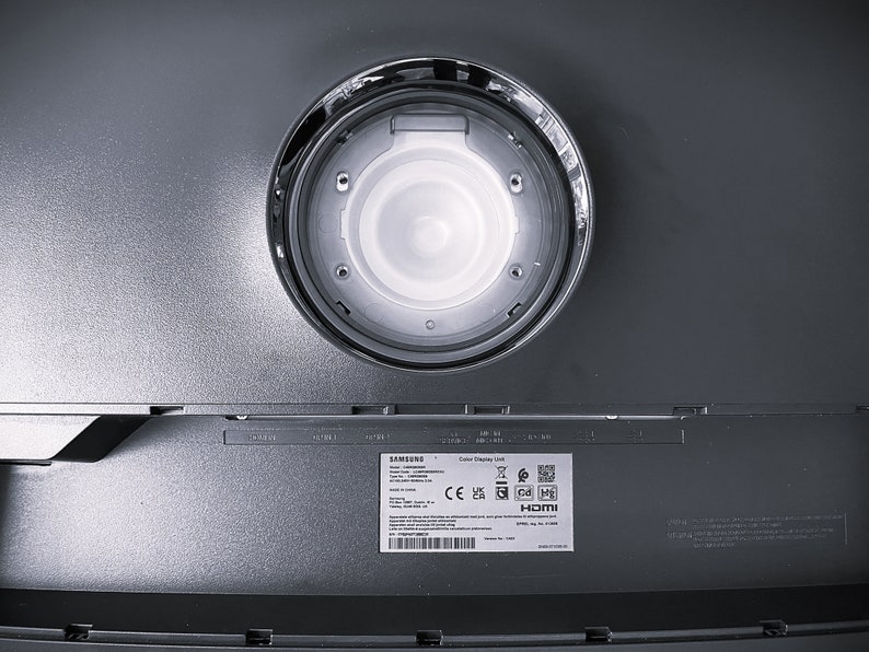 Pu&ograve; includere: Il retro di un'unit&agrave; di visualizzazione a colori Samsung con un'apertura circolare per il montaggio. L'unit&agrave; ha un'etichetta con i loghi CE, UKCA e HDMI.