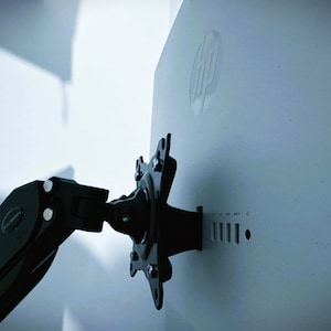 May include: A black monitor arm with a swiveling head attached to the back of a white monitor. The monitor has the HP logo on the back.