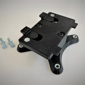 May include: A black plastic phone mount with a base and four screw holes. The mount has two clips on the top to hold a phone in place. There are four silver screws on a white surface.
