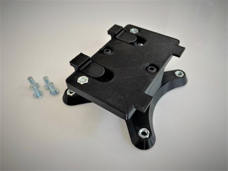 May include: A black plastic phone mount with a base and four screw holes. The mount has two clips on the top to hold a phone in place. There are four silver screws on a white surface.