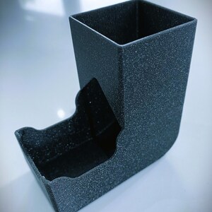May include: A black dice tower with a textured surface. The tower has a square top and a curved bottom.