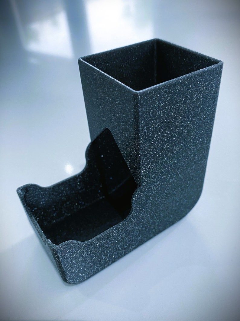 May include: A black dice tower with a textured surface. The tower has a square top and a curved bottom.