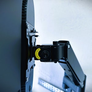 Könnte beinhalten: Schwarzer Monitorarm mit einem gelben Einstellknopf. Der Arm ist an einem schwarzen Monitor befestigt.