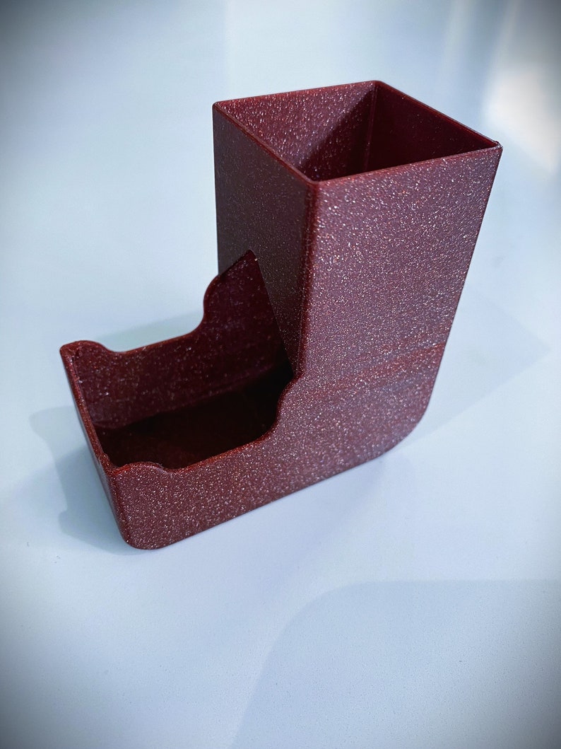 May include: A red dice tower with a textured finish. The tower has a square top and a curved bottom.