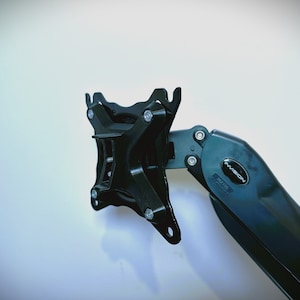 May include: Black metal monitor arm with a swiveling arm and a wall mount. The arm has a black plastic cover with the word "NMEON" printed on it.