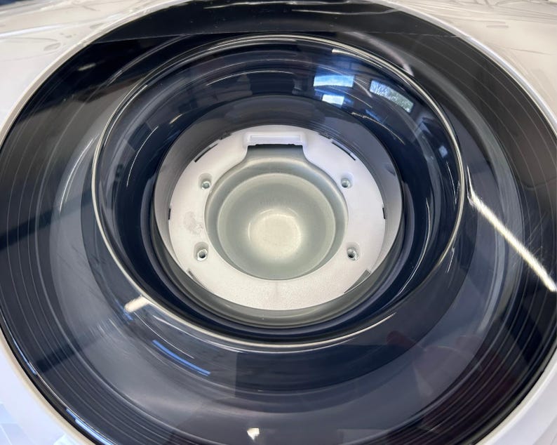 Pu&ograve; includere: Primo piano di un cestello di lavatrice bianco con una guarnizione in gomma nera e un centro in plastica trasparente.