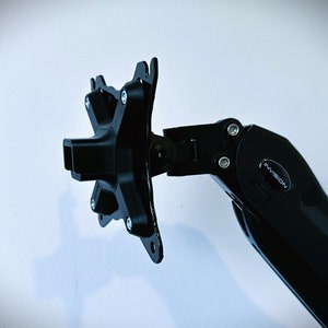 Pode incluir: Bra&ccedil;o de monitor preto com uma base em forma de estrela e um &uacute;nico bra&ccedil;o que se estende para fora. O bra&ccedil;o &eacute; etiquetado como "InVision".