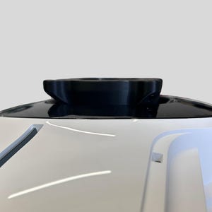 Pu&ograve; includere: Un dispositivo elettronico bianco e arrotondato con una base circolare nera in cima. La base ha una superficie testurizzata.