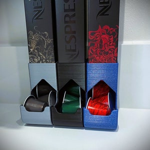 May include: Three black and blue coffee pod holders with the Nespresso logo. Each holder has a slot for coffee pods and is filled with colorful pods.