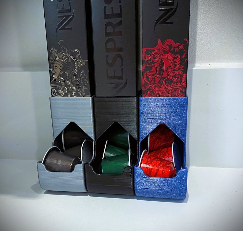 May include: Three black and blue coffee pod holders with the Nespresso logo. Each holder has a slot for coffee pods and is filled with colorful pods.